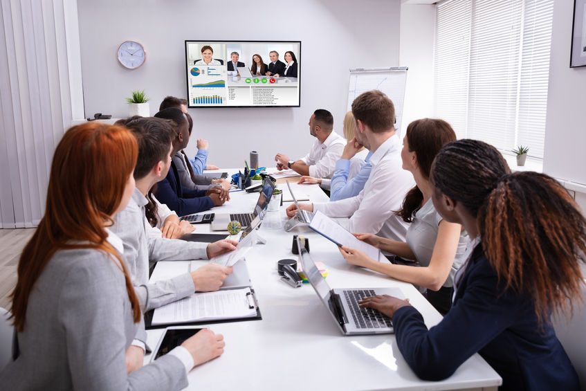 Group Of Businesspeople Having Video Conference With Another Business Team In Office