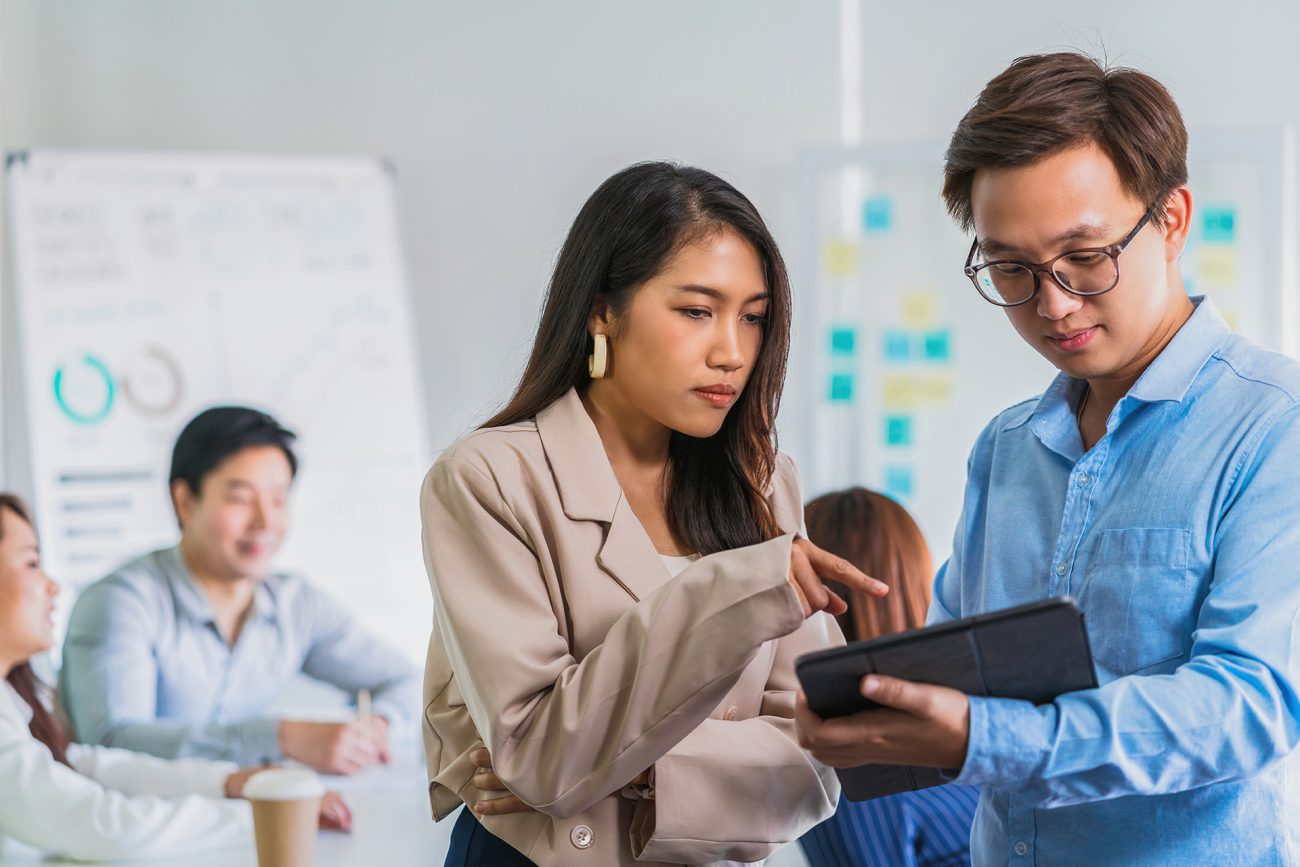 Asian Business colleague working and discussing together with technology tablet over the group of business people brainstorming meeting at workplace, human resource and small business owner concept
